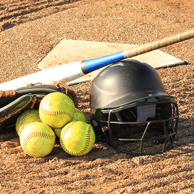 Softball equipment on a baseball diamond including a helmet, bat, and balls.