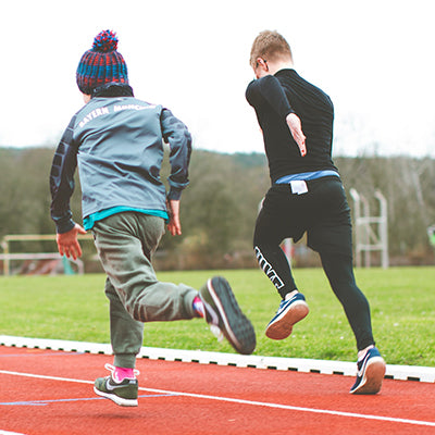Two youth athletes racing on a track and field.
