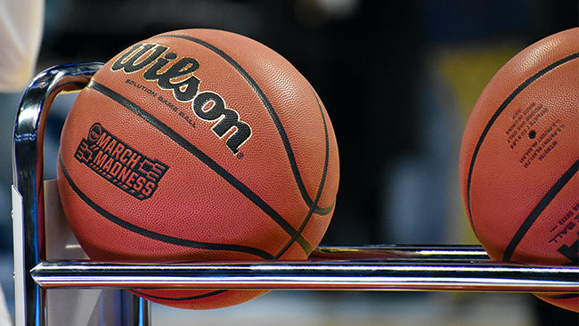 A few Wilson basketballs in a ball cart on a basketball court.