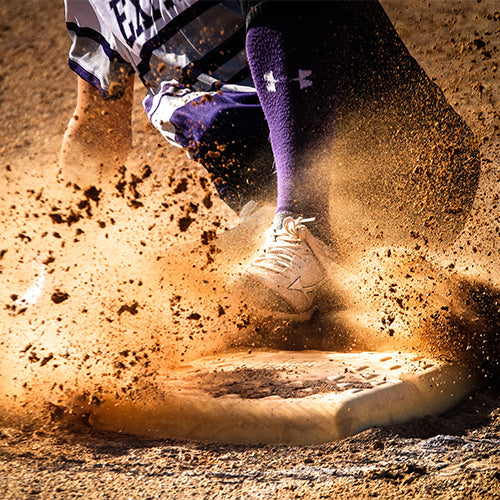 A softball player sliding into a base while kicking up dirt.