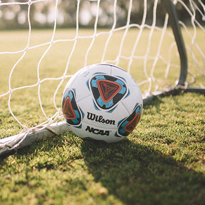 A soccer ball in a goal on a grass field.