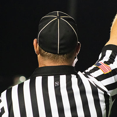 An umpire in a referee uniform with their arm up.